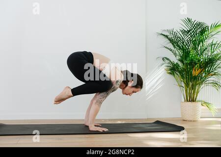 Gut ausgewogene und qualifizierte Frau mit Schulter-Tattoo üben advansed Yoga-Handstände in einem großen Studio. Seitenansicht Stockfoto