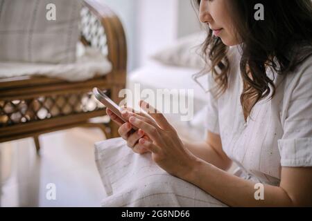 Asiatische Frau, die zu Hause auf dem Boden sitzt, die mobile Anwendung auf dem Handy nutzt oder chattet, Texte liest Stockfoto