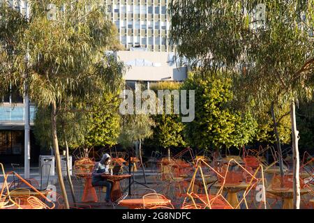 Gestapelt im Freien Möbel, während Studenten studieren draußen auf geschlossenen Café-Terrasse durch covid-19 Sperrbeschränkungen. Stockfoto