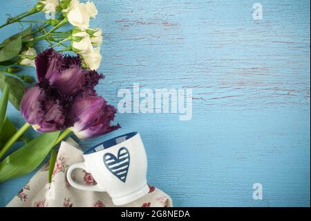 Lila Tulpen, Rosen und Kaffeetasse auf altem blauroten Holzhintergrund. Platz für Text. Stockfoto