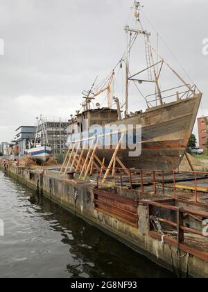 Rostock, Deutschland. Juli 2021. Auf dem Gelände der ehemaligen Neptun-Werft liegen zwei ehemalige Fischkutter an Land. Der ehemalige Fischkutter 'Barth' (l) aus Warnemünde wurde hierher geschleppt und an Land gebracht, weil er kurz vor dem Untergang stand, vor dem ehemaligen Fischkutter 'Wernigerode', der wochenlang auf dem Boden des Stadthafens lag, bevor er gerettet und hierher transportiert wurde. Ob die Fräser verschrottet werden, wird wahrscheinlich noch geklärt, aus wirtschaftlicher Sicht hätten sie wahrscheinlich keine Zukunft mehr. Quelle: Bernd Wüstneck/dpa-Zentralbild/ZB/dpa/Alamy Live News Stockfoto