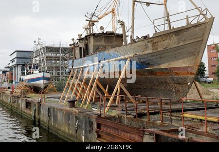 Rostock, Deutschland. Juli 2021. Auf dem Gelände der ehemaligen Neptun-Werft liegen zwei ehemalige Fischkutter an Land. Der ehemalige Fischkutter 'Barth' (l) aus Warnemünde wurde hierher geschleppt und an Land gebracht, weil er kurz vor dem Untergang stand, vor dem ehemaligen Fischkutter 'Wernigerode', der wochenlang auf dem Boden des Stadthafens lag, bevor er gerettet und hierher transportiert wurde. Ob die Fräser verschrottet werden, wird wahrscheinlich noch geklärt, aus wirtschaftlicher Sicht hätten sie wahrscheinlich keine Zukunft mehr. Quelle: Bernd Wüstneck/dpa-Zentralbild/ZB/dpa/Alamy Live News Stockfoto