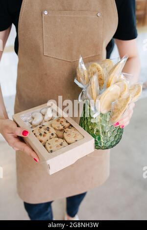 Kekse in einer Fensterbox und auf Stäben in einer Vase, die von einem Konditor in den Händen gehalten wird. Er trägt eine beigefarbene Schürze. Stockfoto