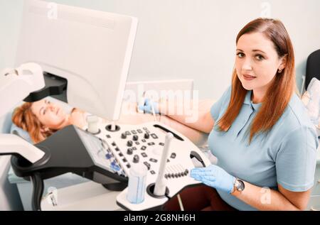 Sonografin mit sterilen Handschuhen, die weibliche Patientin mit einem Ultraschallgerät untersucht. Ärztin bei Ultraschalluntersuchung. Konzept des Gesundheitswesens, ultr Stockfoto