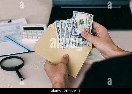 Die Hand eines Mannes hält einen Umschlag mit Geld und zählt Geld amerikanische Dollar. Einkommen, Analyse der Geschäftsfinanzen, Immobiliensteuerkonzept. Stockfoto