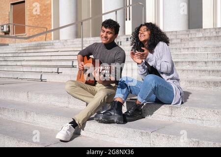 Ein junges lateinisches Paar spielt Gitarre und singt auf einer Treppe. Generation der Millennials. Stockfoto