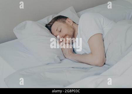 Hübscher junger Mann, der bequem zu Hause im Bett schläft Stockfoto