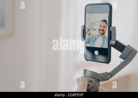 Männliche Hand hält den Gimbal-Stabilisator mit dem Smartphone und lächelt an der Kamera Stockfoto