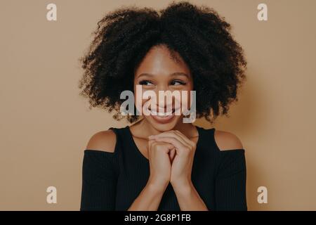 Die Studioaufnahme des glücklichen Afro-Mädchens hält die Hände unter dem Kinn zusammen Stockfoto