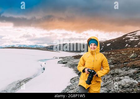 Aurlandsfjellet, Norwegen. Glückliche junge Frau touristische Reisende Fotograf mit der Kamera zu Fuß in der Nähe von Aurlandsfjellet Scenic Route Straße. Aktiven Lebensstil Stockfoto