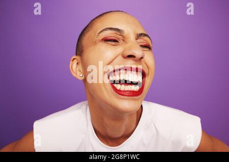 Nahaufnahme der fröhlichen Frau mit bunten Make-up. Komisches Porträt einer weiblichen Model mit Make-up lachend auf grauem Hintergrund. Stockfoto