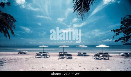 Tropischer Strand mit Palmen, blauem Himmel und Liegestühlen mit Sonnenschirmen. Stockfoto