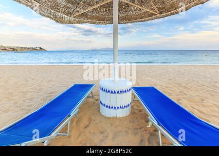 Sonnenschirm und zwei leere Liegestühle am Strand Stockfoto