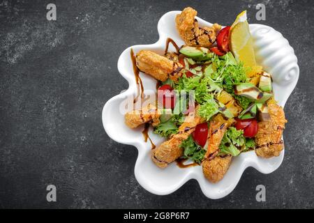 Japanische Küche – Tempura Shrimps-Garnelen in Tempura mit Zitronenscheiben und Salat auf schwarzem Hintergrund Stockfoto