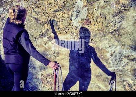 Porträt einer jungen reifen kaukasischen Frau, die mit einem Trekkingstock und ihrem Schatten in einer Fassade steht. Navarra, Spanien, Europa. Stockfoto