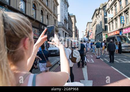 Glasgow, Schottland, Großbritannien. 21. Juli 2021. IM BILD: Zuschauer machen Fotos auf ihren Kameratelefonen, um die Band aufzunehmen, die eine Wiedergabe der Indiana Jones Theme Tune spielt. Dreharbeiten am Set von Indiana Jones 5 mitten im Stadtzentrum von Glasgow, als der Hollywood-Blockbuster Glasgow als New York City aufstellte. Eine vollständige Produktion ist zu sehen, mit einer großen Besetzung, Produzenten und Extras. Das Stadtzentrum wurde so verändert, dass alle Ladenfronten und Gebäude wie 1959 Amerika aussehen. Quelle: Colin Fisher Stockfoto