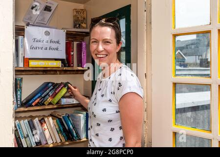 Clonakilty, West Cork, Irland. Juli 2021. Eine alte Telefonbox in der Kent Street in Clonakilty wurde in eine Initiative „Take a Book, Leave a Book“ umgewandelt. Abgebildet ist Aoileann Ní Chomhraí aus Dublin, der ein Buch zum Lesen auswählt. Quelle: AG News/Alamy Live News Stockfoto