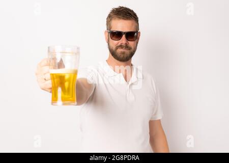 Junger attraktiver kaukasischer Mann in legerer Kleidung, der Sonnenbrille trägt und Bier vor weißem Hintergrund hält. Konzept für Strandurlaub. Stockfoto