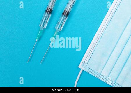 Mehrere Spritze und Gesichtsmaske auf blauem Tisch - Draufsicht. Spritzen sind für die Impfung oder Injektion vorbereitet. Medizinisches Experiment. Blaue Medizinische Einweg-Maske. Virenschutz - Flat Lay Stockfoto