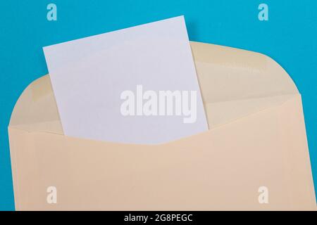 Beigefarbener Umschlag mit leerem weißen Blatt Papier im Inneren, auf blauem Hintergrund liegend - Mock Up with Copy Space. Posteingang oder Benachrichtigung, Postkarte senden - Draufsicht, Flat Lay Stockfoto