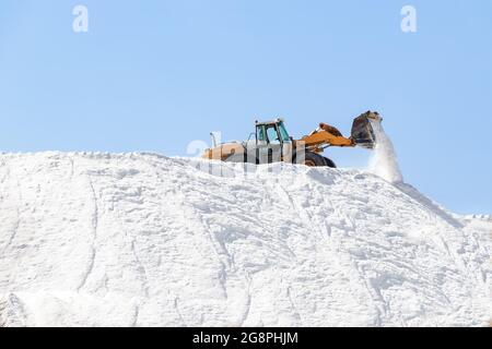 Bagger arbeiten in einem riesigen Salzstapel in Salzwerken. Meersalz, das durch die Verdunstung von Meerwasser entsteht. Stockfoto