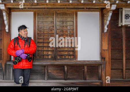 Noboribetsu, Japan-Dezember 22,2017: Junger Mann posiert im Holzhaus mit Handschuh und warmer Jacke bei der Aufnahme von Fotos im Freien während der Wintersaison Stockfoto