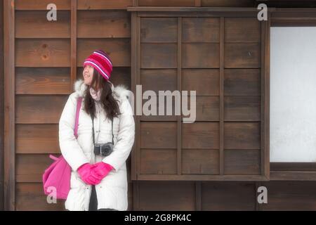 Noboribetsu, Japan-Dezember 22,2017: Junge hübsche Dame posiert im Holzhaus mit Hut, Handschuh und warmer Jacke bei der Aufnahme von Fotos im Freien während des Wints Stockfoto