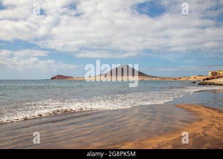 Bewölktes Morgengrauen im El Medano Resort, Blick auf das ruhige Meer mit ruhigen Wellen, die ideale Schwimmbedingungen und den vulkanischen Berg zeigen Stockfoto