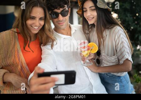 Eine Gruppe lächelnder junger Menschen, die ihr Handy beobachten und gemeinsam Spaß haben. Freunde, die Tech-Konzept verwenden. Stockfoto