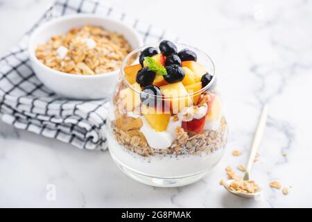 Joghurt mit Müsli und Früchten im Glas auf Marmortisch-Hintergrund. Gesunde Snacks zum Frühstück Stockfoto