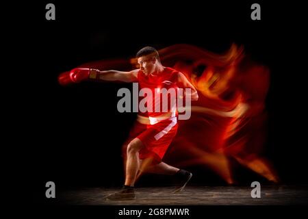 In voller Länge Porträt eines professionellen Boxers üben Schläge über schwarzem Hintergrund in gemischten Lichtern. Seitenansicht Stockfoto