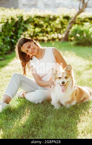 Ein wunderschönes Mädchen kümmert sich um ihren Hund der Corgi-Rasse, der im Sommer an einem sonnigen Sommertag mit einem Kamm ihre Haare kämmt Stockfoto