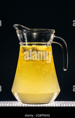 Glaskrug mit erfrischender Limonade, kohlensäurehaltigen gelben Getränken oder Eis auf schwarzem Hintergrund Stockfoto