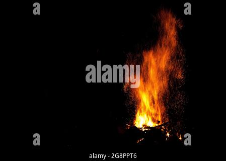 Erstaunliches Lagerfeuer mit wunderschönen gelben und orangenen Flammenanstachelung und einer riesigen Funkenschnur in Form von Tracks auf schwarzem Hintergrund Stockfoto