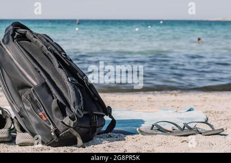 Ein stilvoller schwarzer Rucksack für Reisende am Ufer. Das Konzept von Reisen, Urlaub, Freiheit. Leere tropische Landschaft mit einem Sandstrand am Meer.Cop Stockfoto