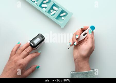 Patientenhände mit Pillen und Pulsoximeter, digitales Fingergerät zur Messung der Sauerstoffsättigung in der Lunge. Reife kaukasische weibliche Hand. Reduziert Stockfoto