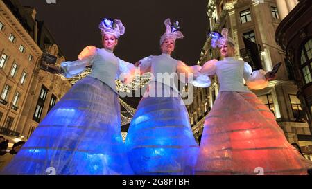 Stelzentänzer treten im Regent Street Christmas Lights Switch On, London, England, in beleuchteten Kleidern auf Stockfoto