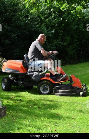 Ein Männchen auf einer Fahrt mit einem Rasenmäher, der an einem Sommertag das Gras schneidet Stockfoto