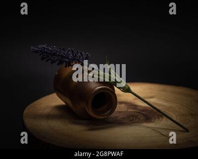 Ein einzelner Lavendelstiel aus Kunstleder und eine alte Flasche vor einem Holz und schwarzem Hintergrund. Stockfoto