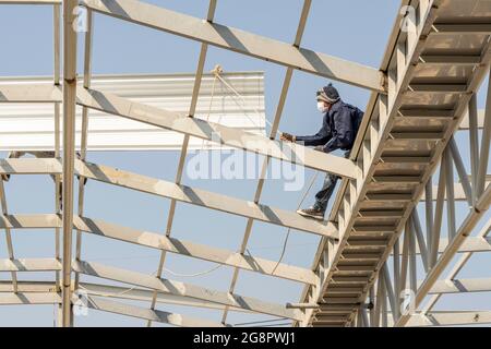 Mann, der an Dachblech auf Leichtstahl-Truss- und Rahmenkonstruktion arbeitet. Stockfoto