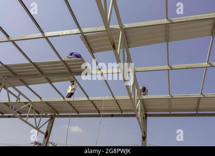 Drei Männer installieren das Dachblech an der leichten Truss- und Rahmenkonstruktion aus Stahl. Stockfoto