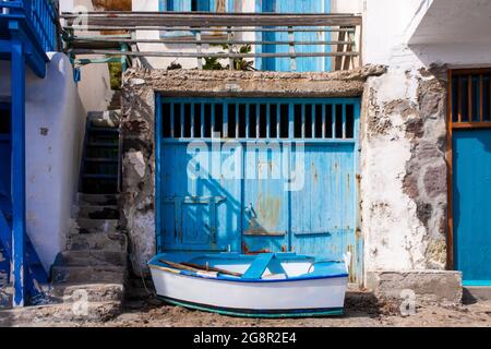 Leuchtend blaue Garagentore mit einem kleinen Holzboot vor dem Fischerdorf Greek Klima - dem buntesten Dorf Griechenlands. Stockfoto