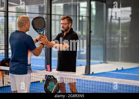 Überwachen Sie den Padel-Unterricht für den Mann, sein Schüler - Trainer lehrt Jungen, wie Padel auf dem Hallentennisplatz zu spielen Stockfoto