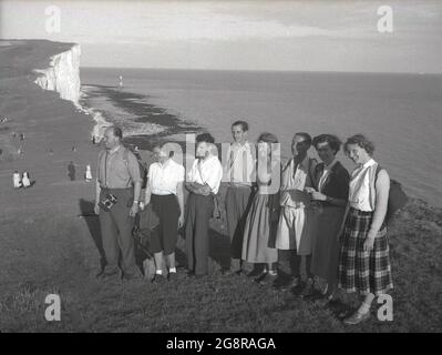 In den 1950er Jahren, historisch, eine Gruppe von erwachsenen Wanderern in Kleidung der damaligen Zeit, auf den Südhängen in Beachy Head, in der Nähe von Eastbourne, East Sussex, England, Großbritannien. Die Umgebung ist die höchste kalkartige Meeresklippe Großbritanniens und berühmt für ihre Spazierwege mit herrlichem Blick auf den Ärmelkanal. In der Ferne kann man in der Bucht den 1902 erbauten Offshore-Leuchtturm sehen - den letzten in Großbritannien. Stockfoto