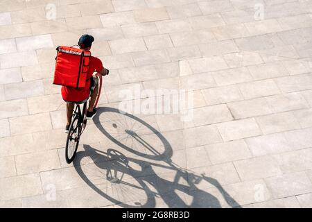 Afrikanischer Lieferer mit Mütze auf dem Fahrrad in der Stadt, um ein Paket zu liefern. Stockfoto