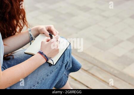Nahaufnahme einer jungen Rotschopf-Frau, die im Freien in einem Notizbuch schreibt Stockfoto