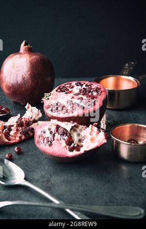 Granatapfel mit Samen Messbecher und Löffel auf schwarzem Hintergrund Stockfoto