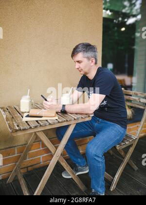 Ein erwachsener Mann sitzt an einem Kaffeetisch und liest am Telefon Stockfoto
