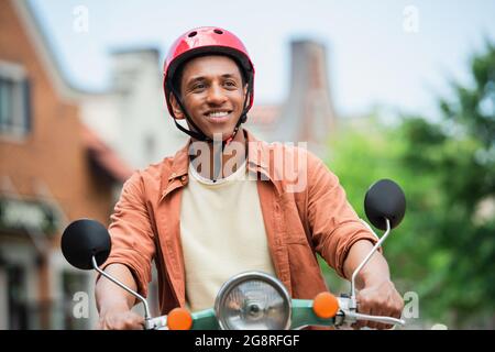 Happy african american Mann in Hardhat genießen Reiten Roller im Freien Stockfoto