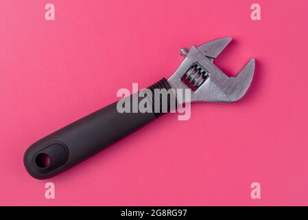 Verstellbarer Schraubenschlüssel mit schwarzem Griff isoliert auf rosa Hintergrund Stockfoto